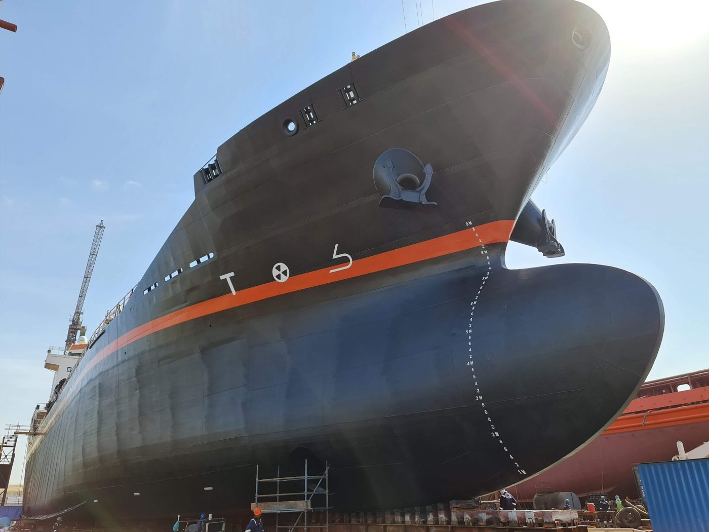 Ship hull in dry dock with a dark hull, orange boot-top stripe and bulbous bow